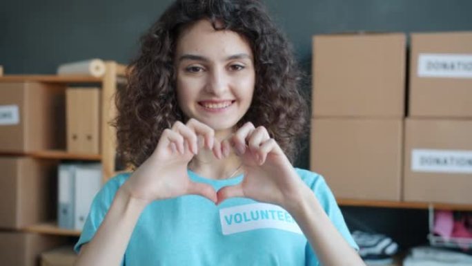 快乐年轻女子志愿者在慈善公司办公室做心脏手势和微笑的慢动作肖像