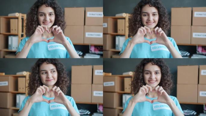 快乐年轻女子志愿者在慈善公司办公室做心脏手势和微笑的慢动作肖像