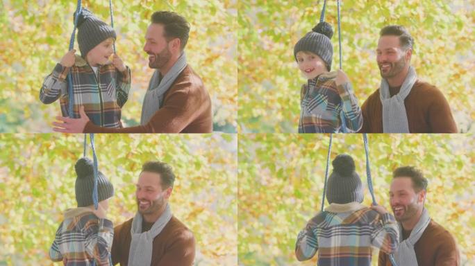 父亲推着儿子在秋季花园的绳索秋千上玩得开心
