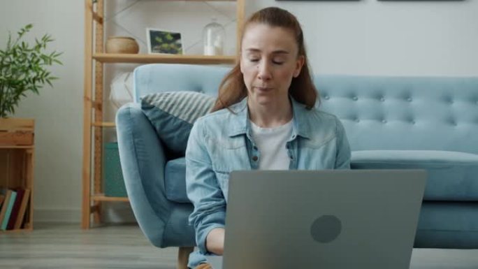 年轻的女性自由职业者与笔记本电脑一起工作，想着看着坐在家里地板上的屏幕
