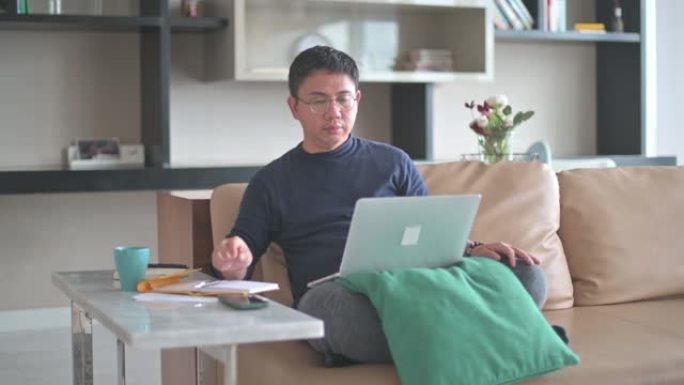 亚洲中国男性在家工作，在客厅沙发上使用笔记本电脑视频通话