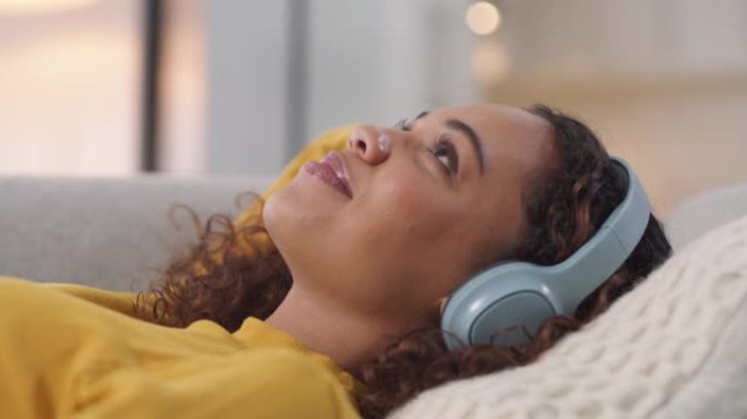 一名年轻女子在家中沙发上使用耳机的4k视频片段