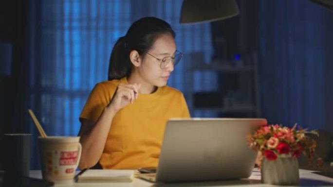 亚洲妇女坐在家里的办公桌上，深夜用笔记本电脑工作