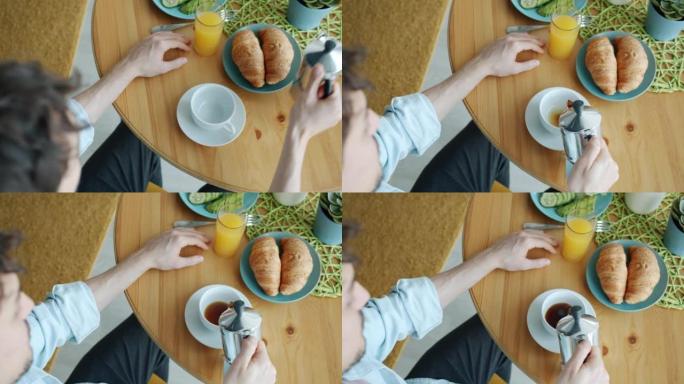 在家吃早餐时，男人的手在杯子里倒咖啡的俯视图