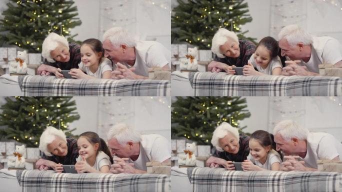 快乐的爷爷奶奶和小女孩在圣诞节看手机