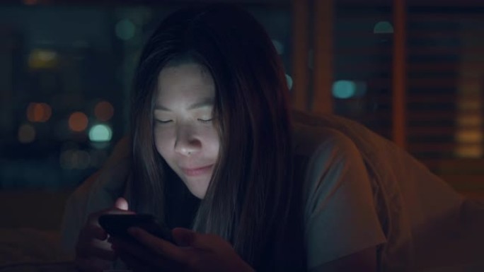 bokeh light city夜间在床上使用智能手机的亚洲女性