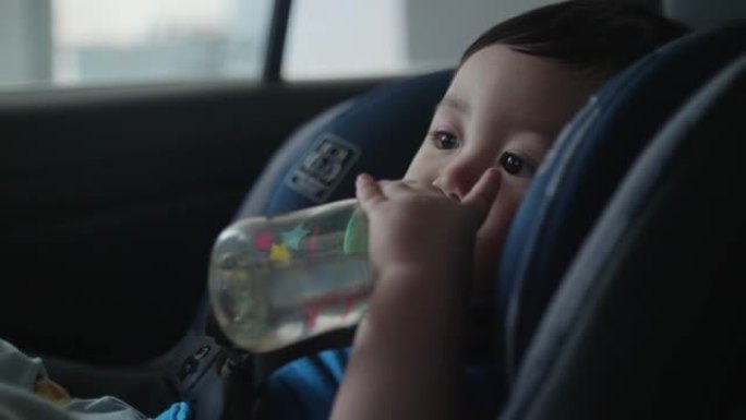 小男孩从汽车座椅上的瓶子里喝水