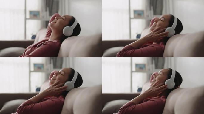 亚洲女性躺在家里的沙发上听音乐放松，慢动作