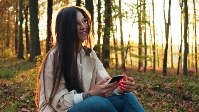 年轻女子坐在森林里，在森林里使用手机