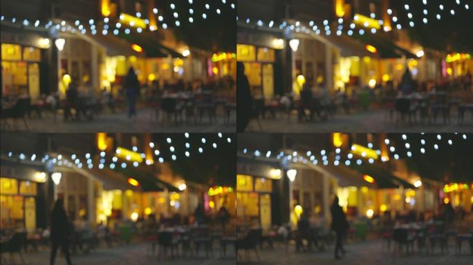 带咖啡馆和夏季露台的照明街道的慢动作拍摄。人们沿着老城的步行街走，选择一个聚餐的地方。舒适的餐厅度过