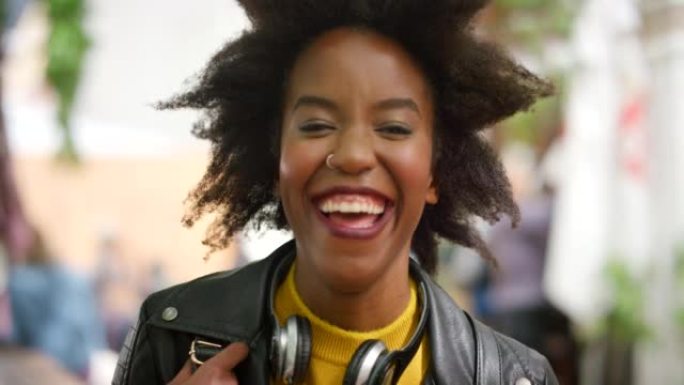 一个快乐、时尚的女人独自在城市里通勤时笑的特写肖像。一位美丽，前卫的黑人女性的头像，非洲裔大笑，看上