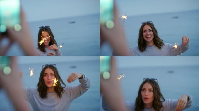 一个快乐的女人在海滩上玩烟火，拍照。一名妇女为她的朋友玩烟火拍照