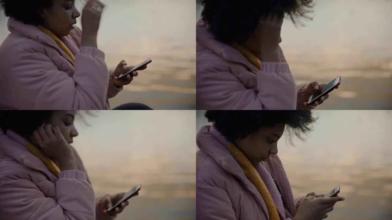 黑人女士在河边使用智能手机时看起来很担心
