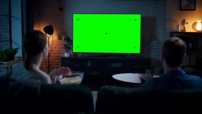 年轻的夫妇花时间在家里，坐在沙发上，在他们时尚的阁楼公寓里看绿屏模拟显示的电视。男人和女人流电影或表
