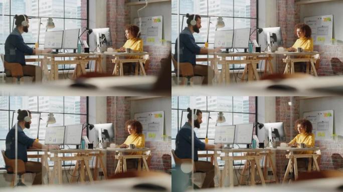 男人和女人坐在大窗户旁边的桌子后面，可以看到城市景观，并在计算机上处理分析数据。两位多元文化的同事忙