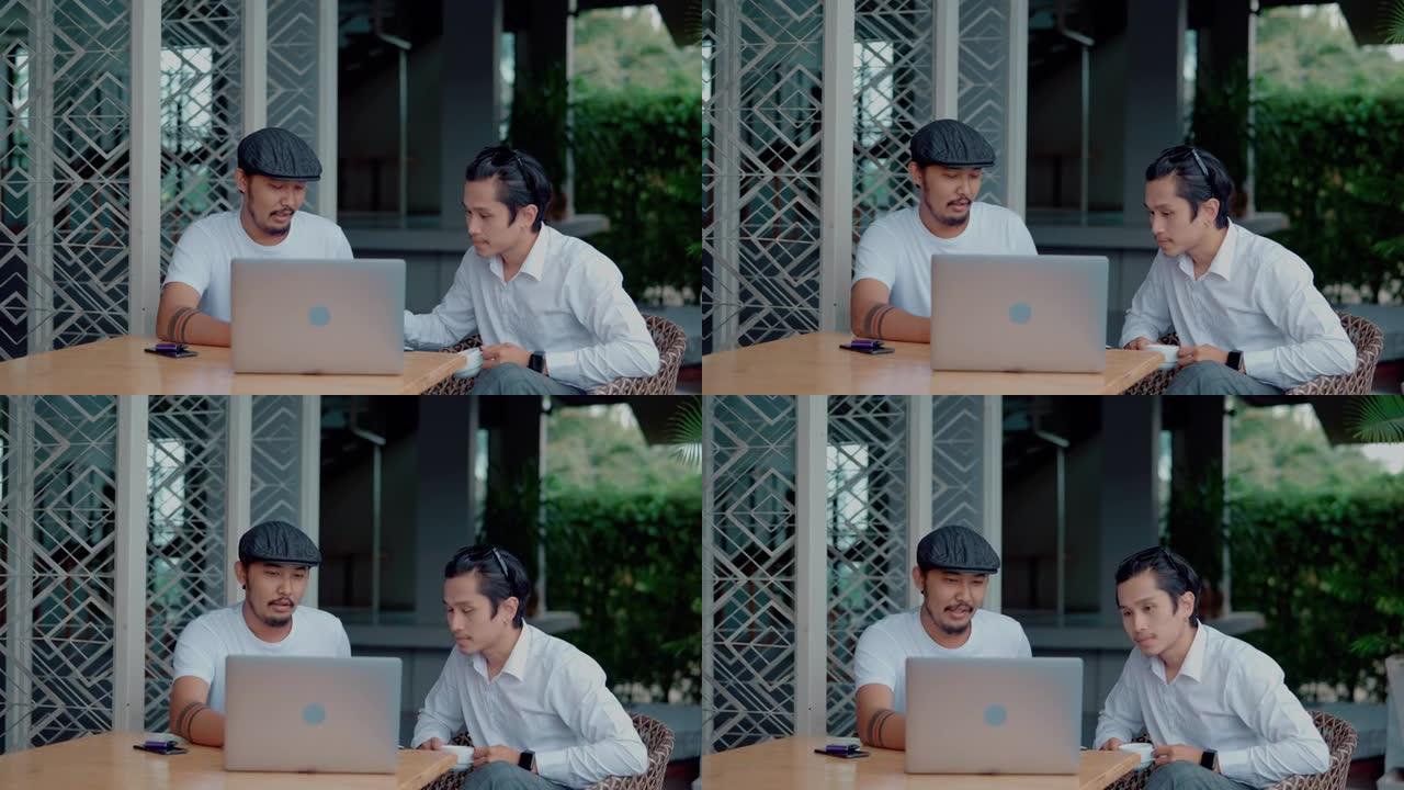 两个亚洲同事坐在餐桌旁，在户外咖啡店用笔记本电脑工作。