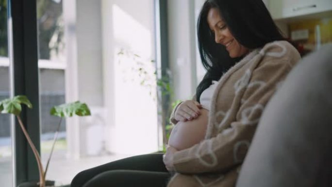 DS怀孕后期快乐的女人坐在家里的沙发上爱抚着她的肚子