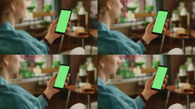 男子拿着智能手机，绿屏模拟显示。男性正在家里休息，在移动设备上观看视频和阅读社交媒体帖子。特写镜头。