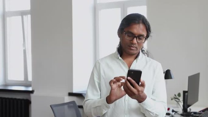 印度商人在办公室工作日使用智能手机戴眼镜