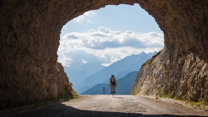年轻的公路自行车手骑在山口上，穿过岩石隧道