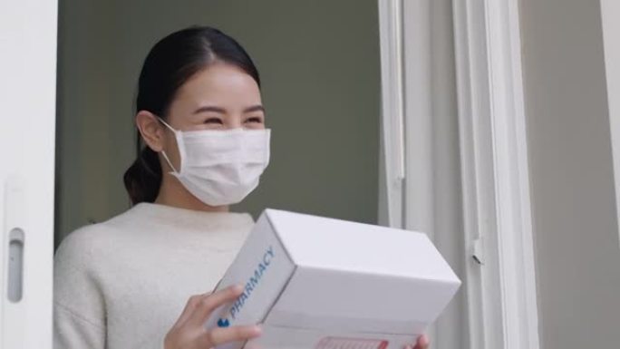 年轻迷人美丽的亚洲女性接受药品包装箱免费从药房医院送急救服务在家戴手套，口罩在远程保健，远程医疗在线