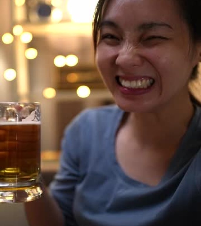 亚洲女性在视频电话会议上与朋友进行欢乐时光，手里拿着啤酒，垂直