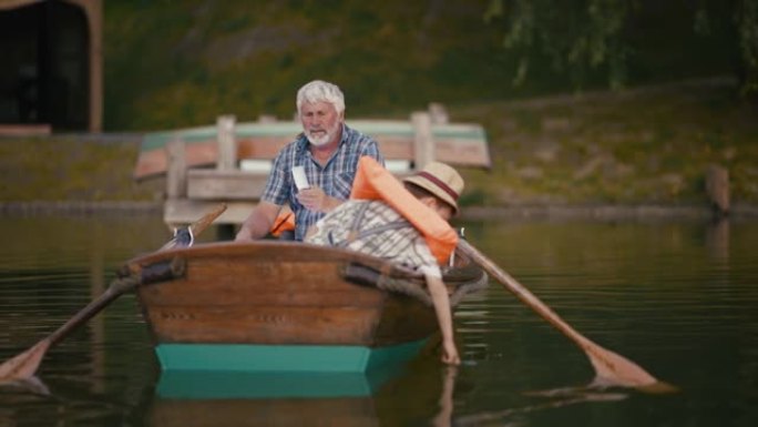 祖父拿着手机与孙子坐在划艇上