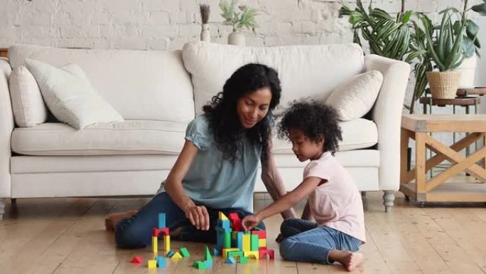 非裔美国母亲和学龄前的女儿在地板上玩构造游戏