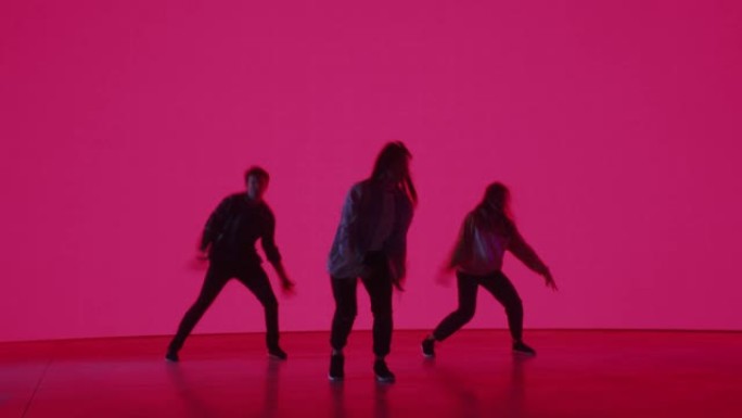 由三位时尚的专业舞者组成的多元化小组，在工作室环境中的虚拟制作过程中，在带有粉红色背景的大Led墙屏