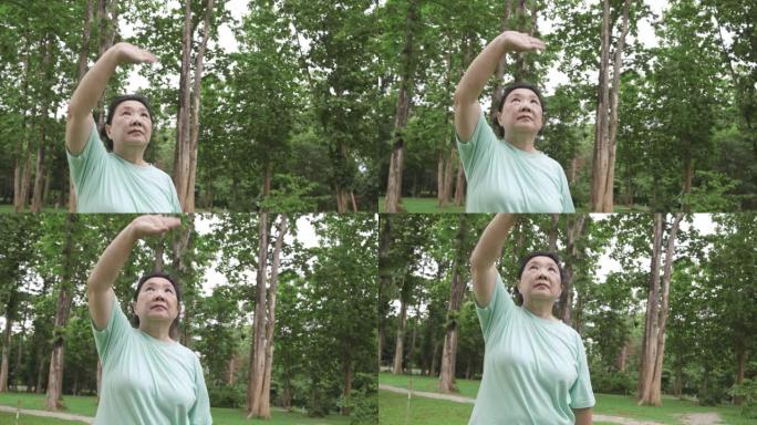 POV手持中枪: 亚洲高级女子在公园跑步后为手臂和肩膀做太极运动。老运动女人把手伸出来，发抖。早上感