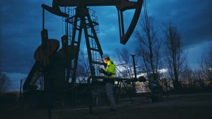 SLO MO石油工人一边使用智能手机，一边检查抽油机上的仪表