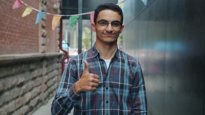 阿拉伯帅哥微笑着在户外展示竖起大拇指手势的慢动作肖像