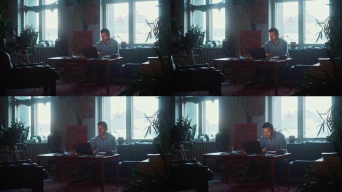 年轻英俊的男人坐在沙发上，在正宗的阁楼办公室的创意机构工作笔记本电脑。翻新的时尚装饰，配有室内植物、