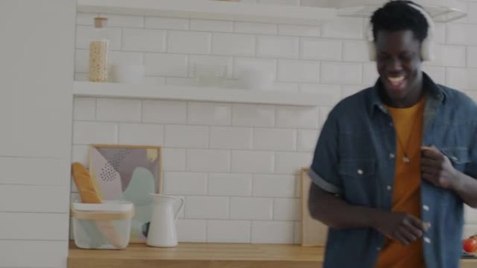 兴奋的非洲裔美国人在家里的厨房里跳舞，通过耳机欣赏音乐
