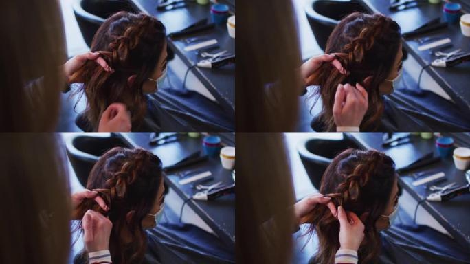 女性美发师在美发沙龙戴口罩的女性顾客编织头发