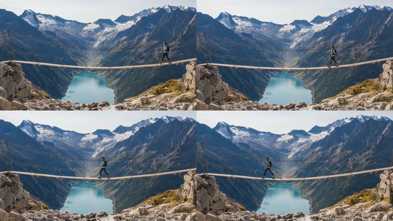 女徒步旅行者在山涧上方的吊桥上行走，欣赏山谷湖和周围山脉的壮丽景色