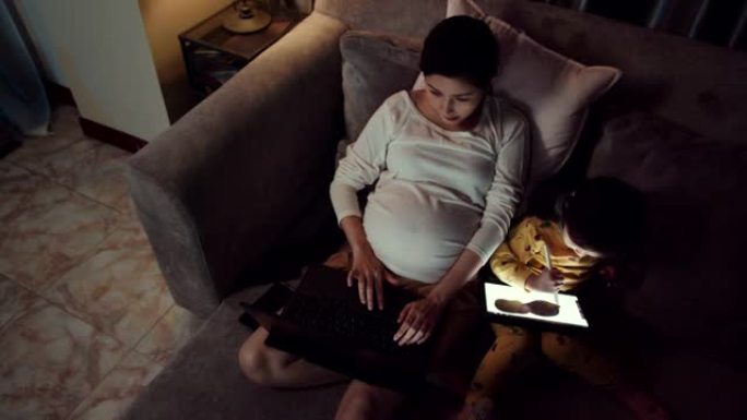 迷人的怀孕母亲工作，而女儿晚上使用数字平板电脑。