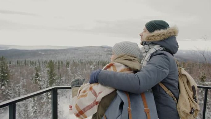 男人和女人在观景台上拥抱并观看令人叹为观止的景色，并在冬天聊天