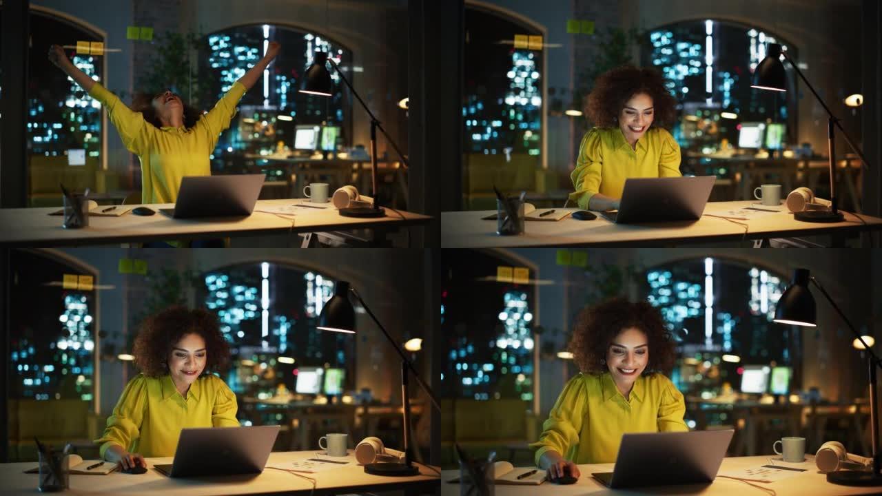 成功的阿拉伯女性坐在创意机构，晚上在笔记本电脑上工作。经理庆祝令人印象深刻的销售业绩。兴奋的专家对她