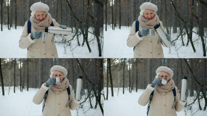 美丽的高级女人在冬季公园愉快的散步时用热水瓶喝茶
