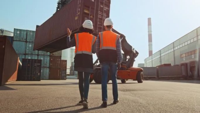 拥有平板电脑的多种族女工业工程师和戴着安全帽和橙色高能见度背心的男工头工人在集装箱码头行走。同事谈物