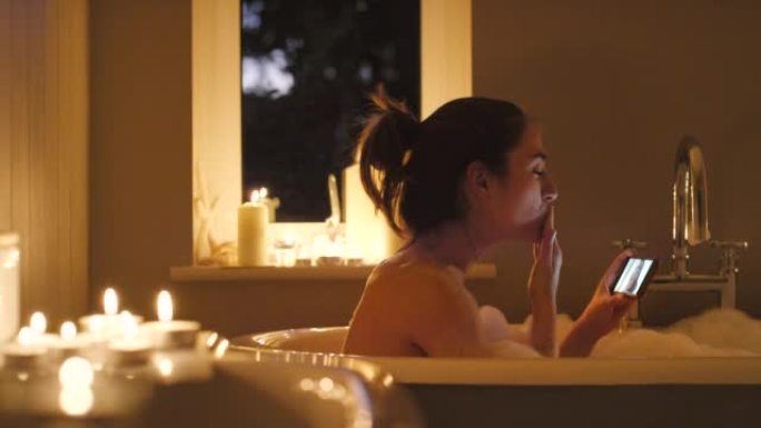 4k视频片段，一名年轻女子在晚上泡泡浴期间进行视频通话