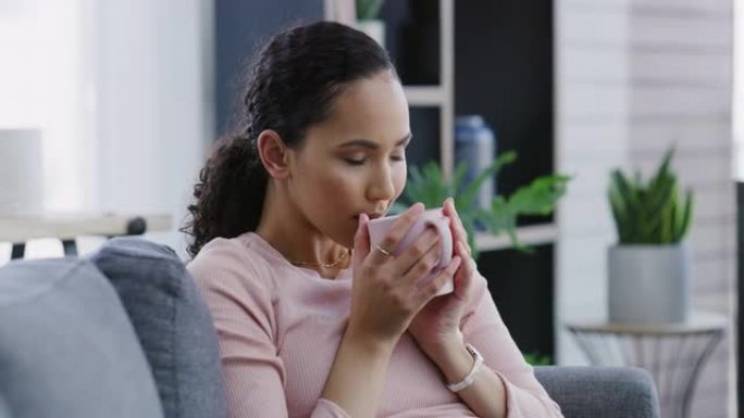 4k视频片段，一名年轻女子独自坐在家里的沙发上，享受一杯咖啡