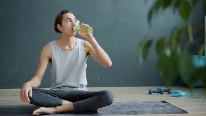 健康的年轻人瑜伽学生从瓶子里喝水，然后看着相机微笑