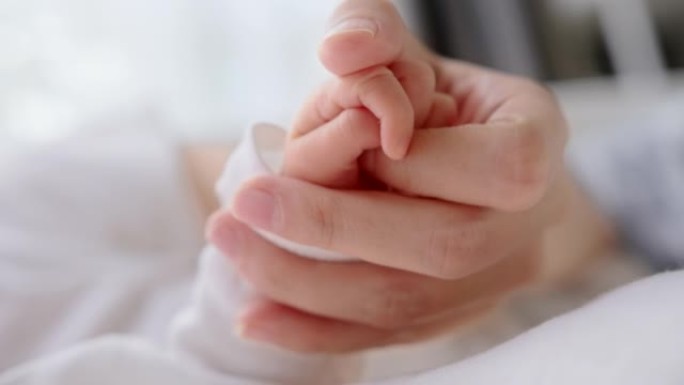 特写新生婴儿在家睡觉时握着母亲的手指。保险人寿、护理、保障