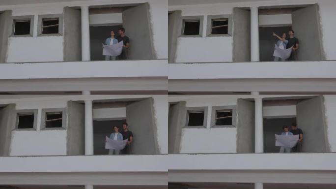 拉丁美洲成年幸福夫妇站在正在建造的房屋的二楼，拿着蓝图，指着远处
