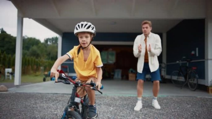 年轻的父亲教儿子在他们大居民区家的草坪上骑自行车。成功的男孩戴着头盔，在自行车上保持平衡和踩踏板。手