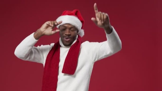 一个戴着圣诞帽和羊毛针织毛衣的黑皮肤男人在红色背景上跳舞
