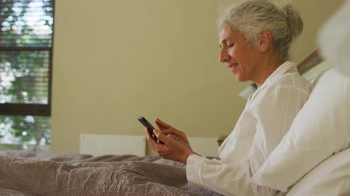 资深混血女子躺在床上，使用智能手机微笑