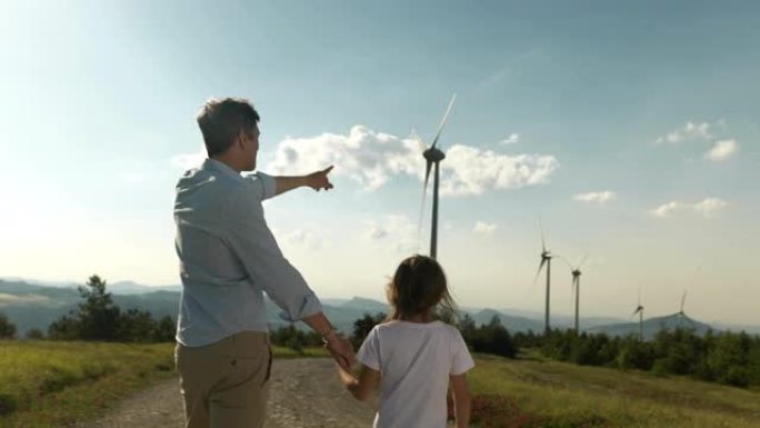 父亲和小女儿手拉手走在风电场中的背景。他们参观了一片绿地，并指向风力涡轮机。可持续的可再生能源确保我